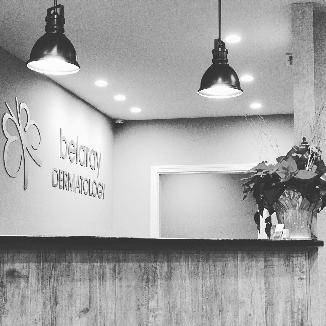 The reception desk inside Belaray Dermatology, with the brushed-metal butterfly logo on the wall